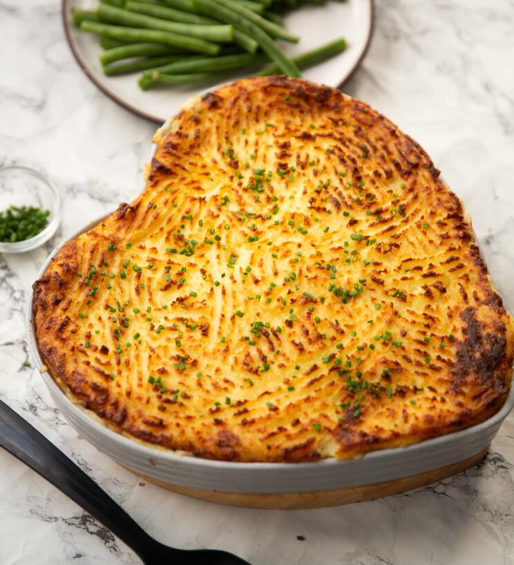 classic fish pie served in heart shaped baking dish with green beans in background