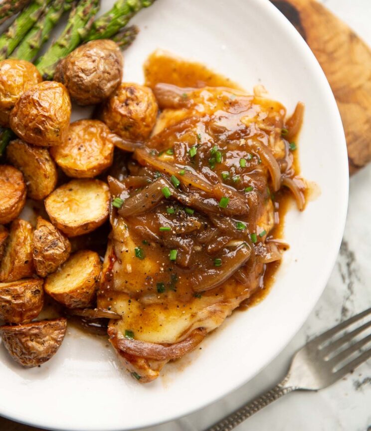 close up overhead shot of french onion chicken breast on small white plate with potatoes and asparagus