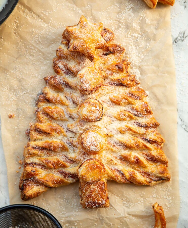 overhead shot of puff pastry Christmas tree on brown baking paper dusted with parmesan