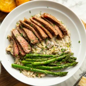 creamy garlic mushroom orzo and steak served in white bowl with asparagus