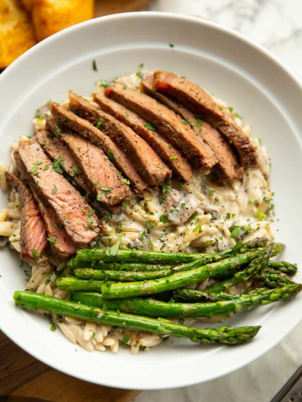 creamy garlic mushroom orzo and steak served in white bowl with asparagus