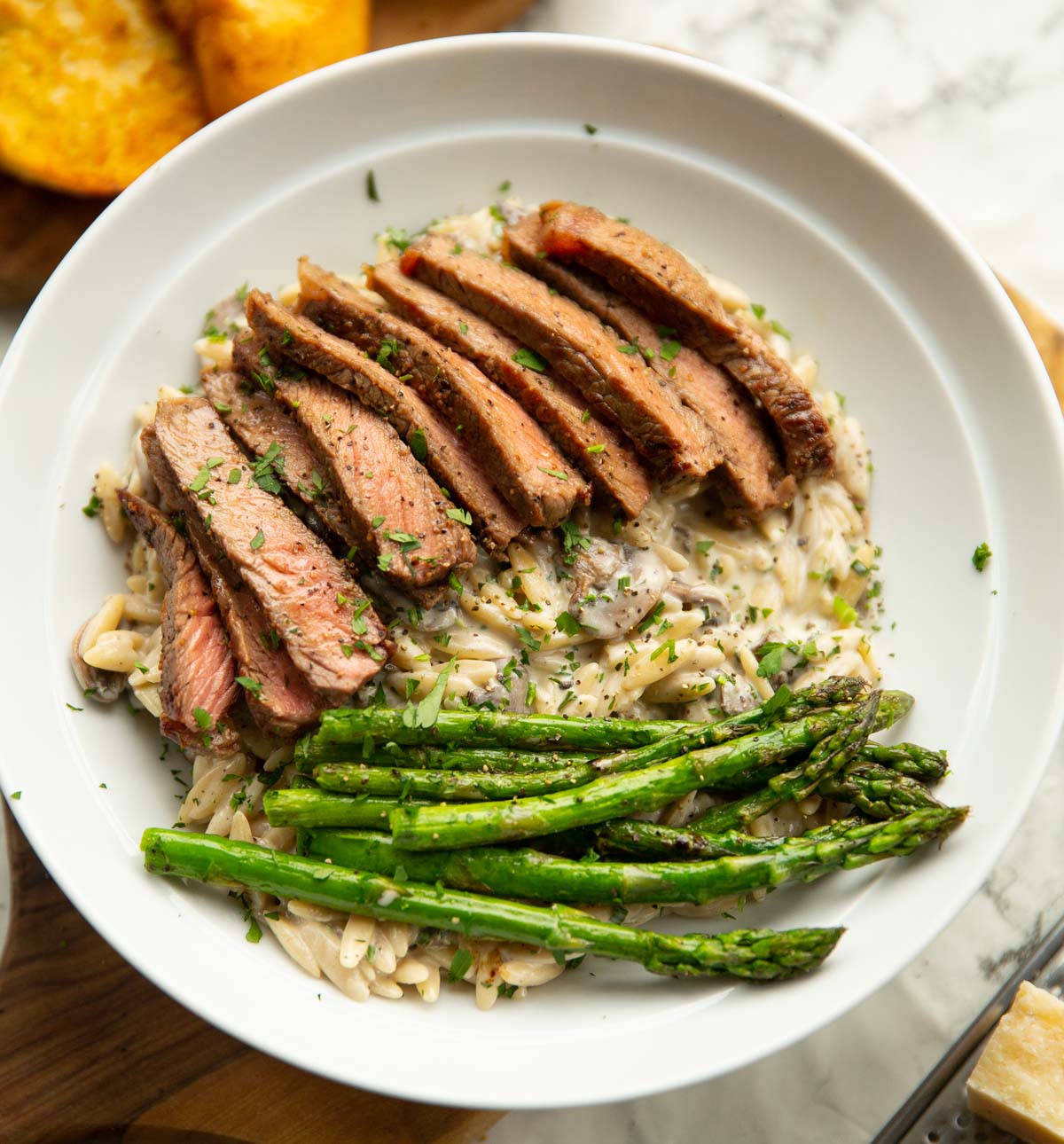 creamy garlic mushroom orzo and steak served in white bowl with asparagus