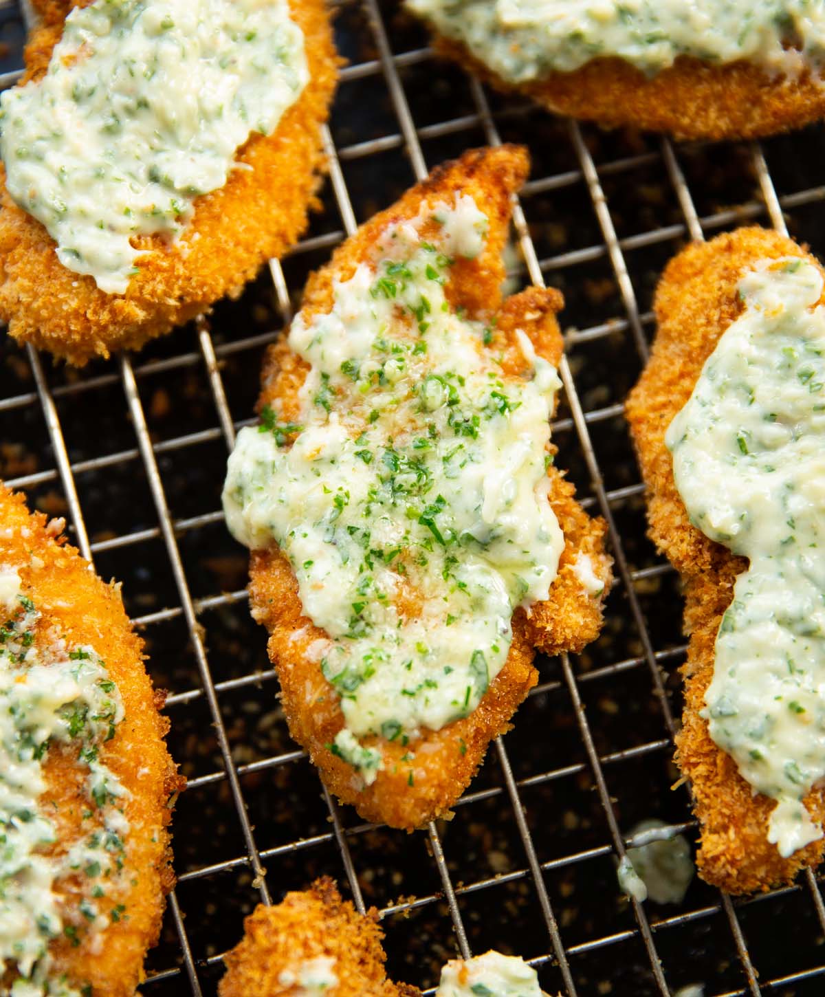 close up shot of garlic butter parmesan chicken tender on wire rack above black tray