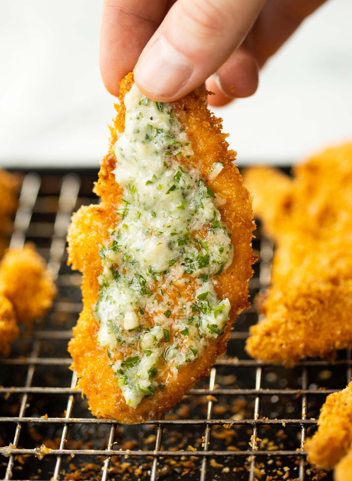 close up shot of hand holding garlic parmesan chicken tender above wire rack