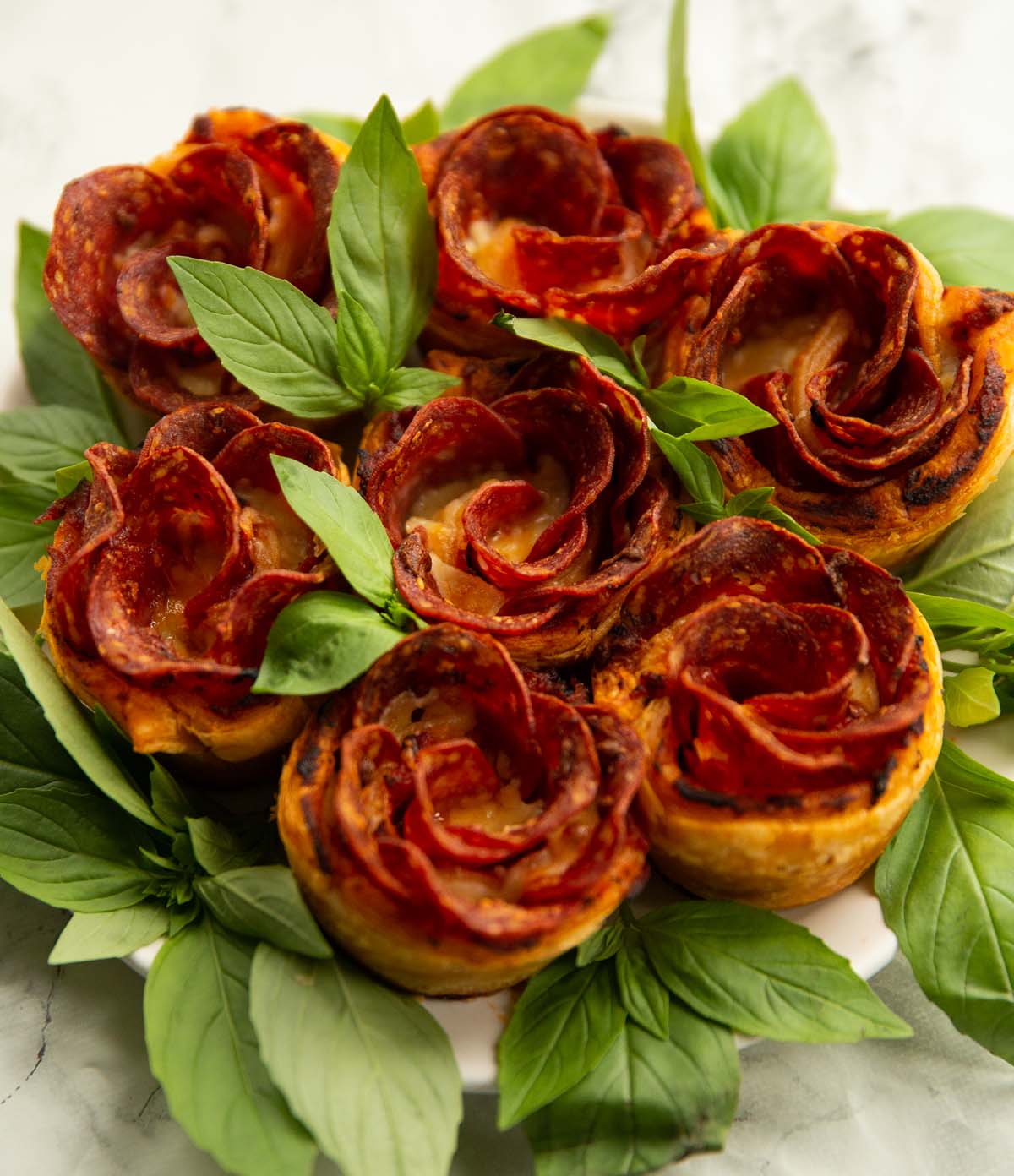 pepperoni pizza roses on small white plate with fresh basil