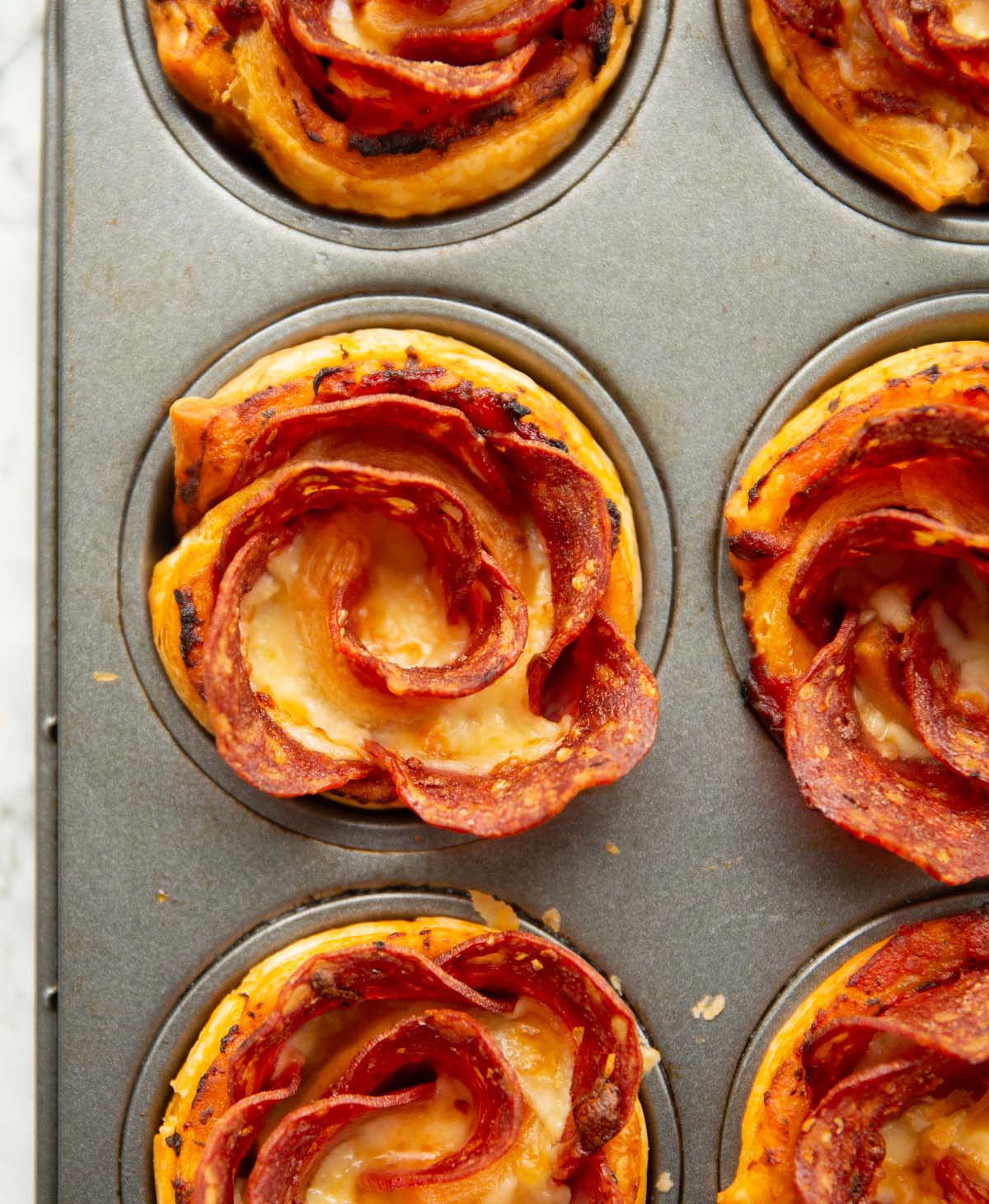 close up overhead shot of pepperoni puff pastry roses in muffin tin