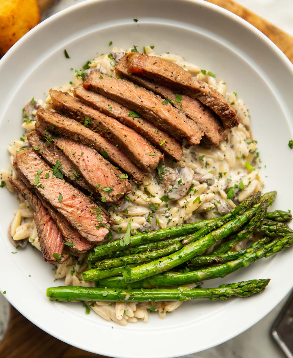 steak with creamy mushroom orzo in white bowl with asparagus