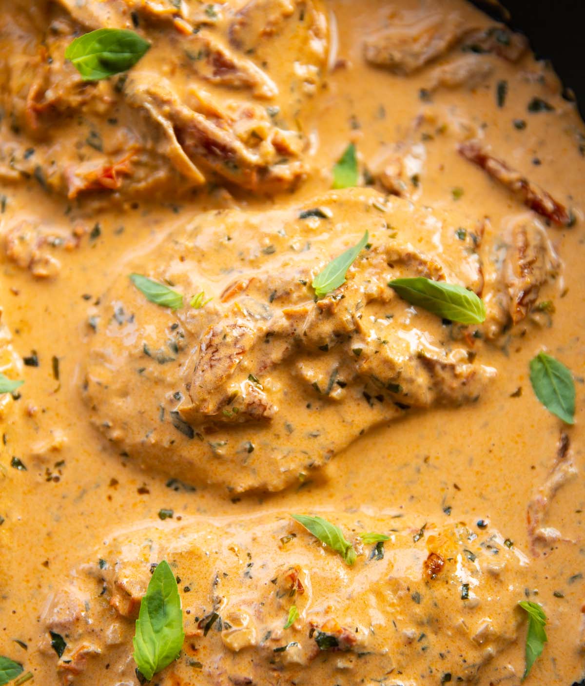 overhead shot of creamy sun dried tomato chicken in pan garnished with fresh basil