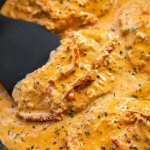 close up shot of spatula lifting sun dried tomato chicken in pan