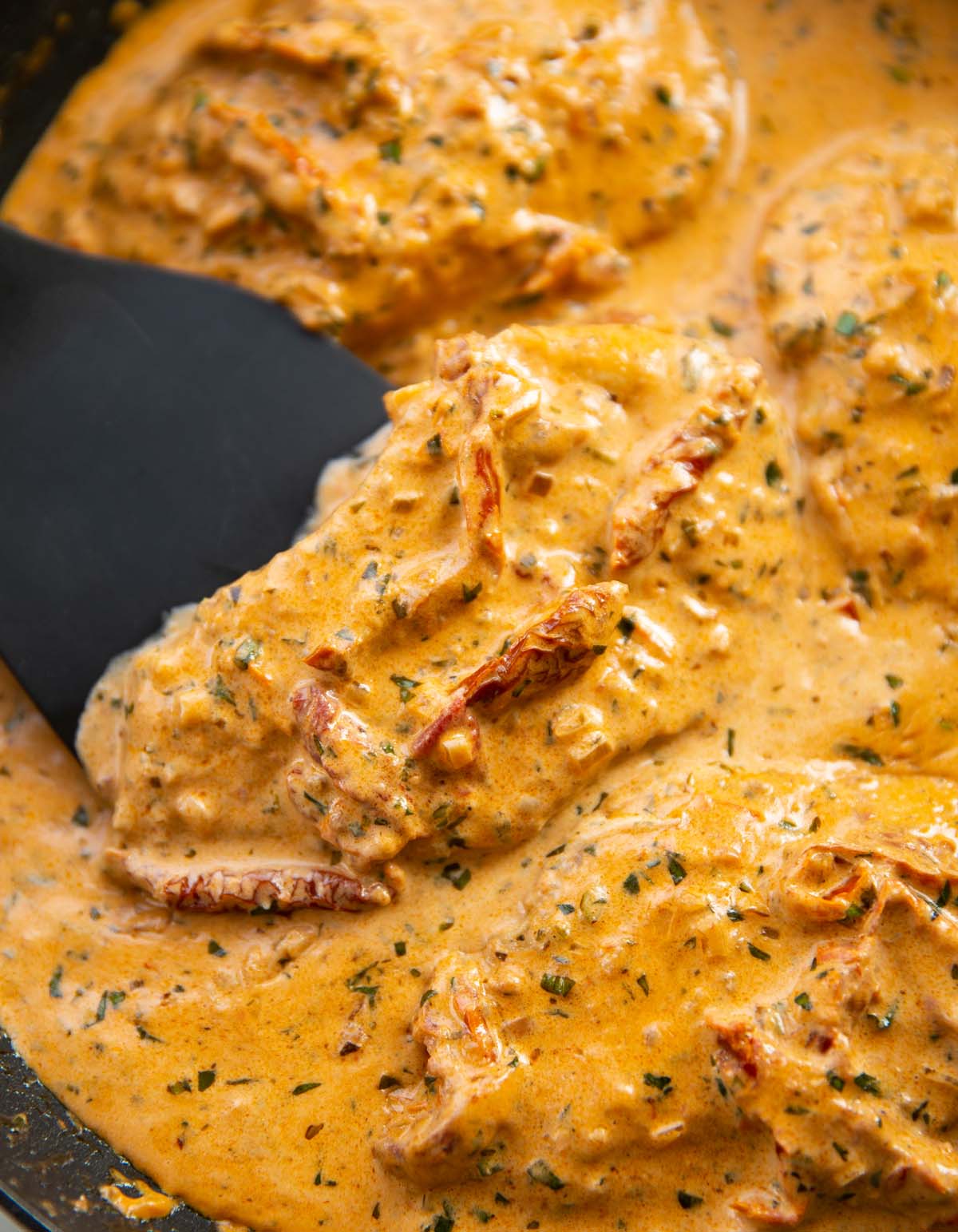 close up shot of spatula lifting sun dried tomato chicken in pan